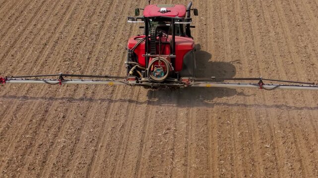 Tractor Spraying Field: A red tractor with extended spray arms cultivates a large field, applying treatment to the soil.