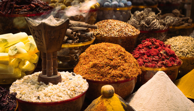 Vibrant close-up of traditional spice market stall with incense burner, featuring piles of saffron, turmeric, rose buds, and aromatic spices, Middle Eastern souk, Old Dubai, UAE