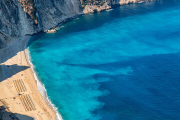 Fototapeta premium Top view aerial drone photo of Myrtos beach with beautiful turquoise water, sea waves and straw umbrellas. Vacation travel background. Ionian sea, Kefalonia Island, Greece