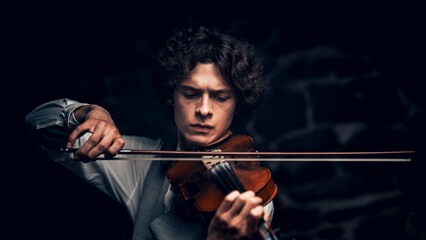 Fototapeta premium Young male violinist playing violin in elegant attire