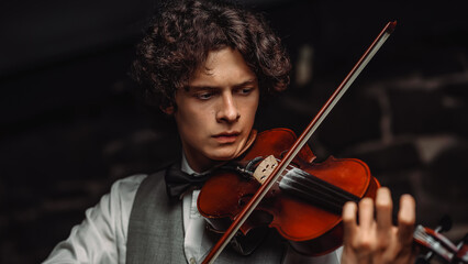 Fototapeta premium Young male violinist playing violin in elegant attire