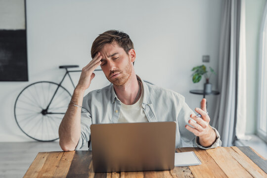 Frustrated man working from home with laptop holding his head in a modern home office
