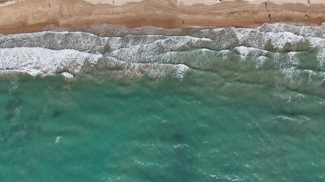 Aerial top view of ocean waves hitting sandy beach coastline