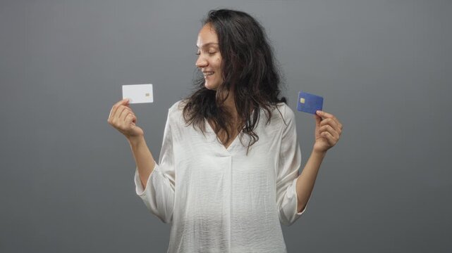 Woman holding two creditcards with hands, smiling and comparing cards in studio; financial choice calm.