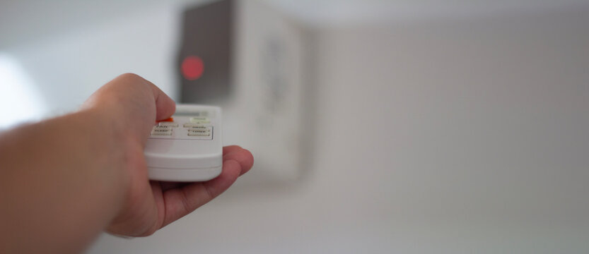 Horizontal defocused photo banner with selective focus. Man regulates temperature at home. Male hand holds air conditioner remote control, presses climate change button. Real estate, rent. Copy space
