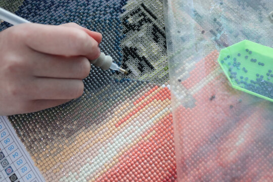 Process of creating diamond painting, child's hands placing small shiny rhinestones on adhesive canvas, creative hobby and craft at home.