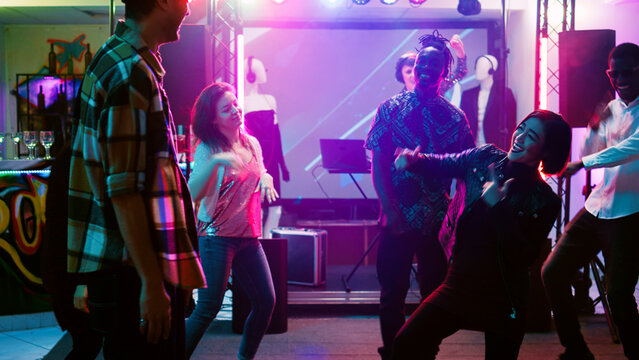 Cheerful adults dancing at disco party, having fun at social gathering on dance floor. Modern funky people showing cool dance moves on live music at nightclub, entertainment. Handheld shot.