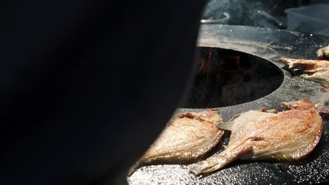 Fresh fish grilling on a hot metal plate over an open fire. Assorted seafood cooking on a barbecue. Traditional outdoor street food preparation and rustic summer picnic cooking concept.