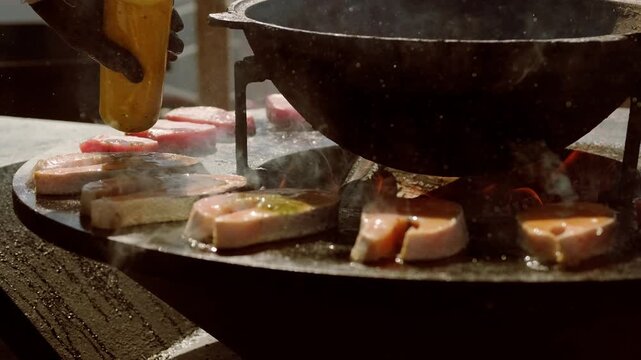 Chef cooking salmon steak on outdoor grill with open flames. Professional grilling process of fish fillet. Culinary event, street food preparation and gourmet seafood cooking technique.