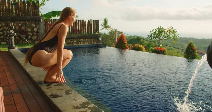 Smiling woman tests water temperature of infinity pool in Nusa Penida Bali resort