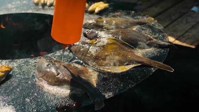 Fish grilling on hot outdoor metal stove. Whole flounder cooking over open fire with smoke. Summer barbecue picnic scene. Seafood preparation on rustic grill in garden. Delicious meal.