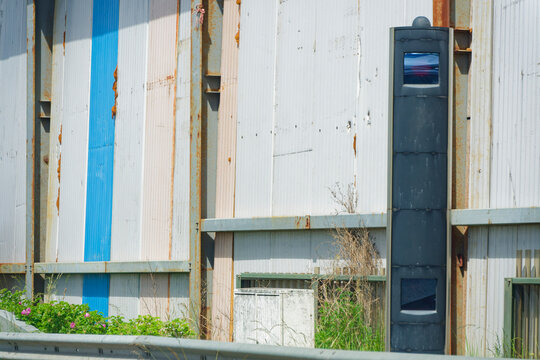 Rusty metal wall with blue stripe and black traffic speed camera on roadside A7 E45 Germany
