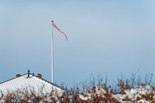Snow covered roof with a flagpole and a red Danish Flag Danebrog Dannebrog on a clear winter day