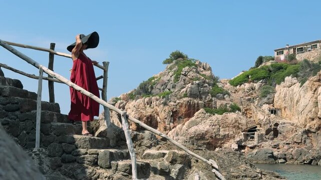 Woman walking stone stairs overlooking Cala Deia cove in Mallorca, Spain