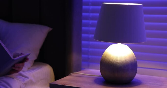 Woman turning on night lamp and taking book on bed at home, closeup. Camera moving forward