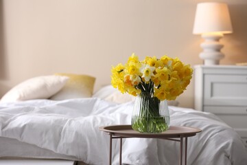 Beautiful daffodil flowers in vase on table near bed indoors, space for text © New Africa