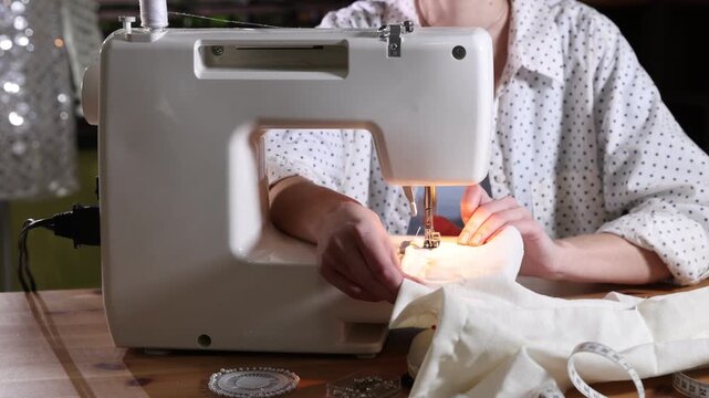 Woman sewing fabric with professional machine at wooden table in workshop, closeup