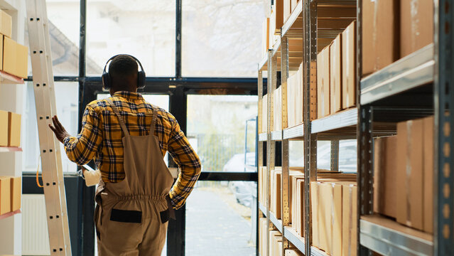 Funny guy showing dance moves in storage room, employees laughing at colleague dancing. Young person acting silly listening to music on headphones, working in warehouse space.