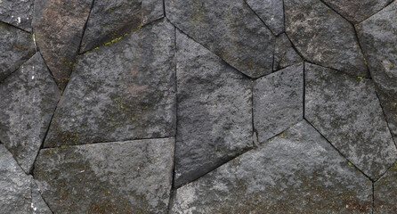 Obraz premium Weathered dark gray stone wall with intricate polygonal masonry pattern; ancient outdoor surface texture background