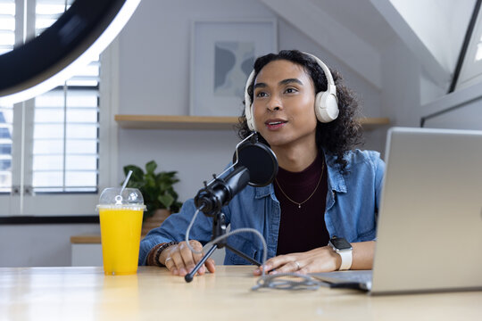 Non-binary adult creator in denim jacket and headset, speaking into mic with laptop in home studio
