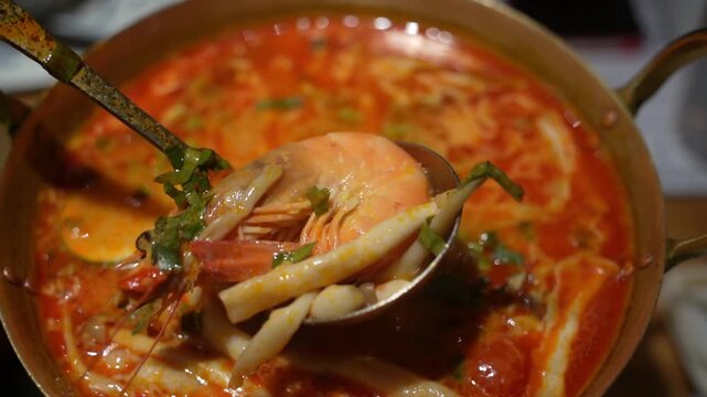 Close-up of a spoon dipping into a rich and flavourful Tom-Yum Goong seafood soup, made with a spicy tomato broth and loaded with fresh fish and shellfish