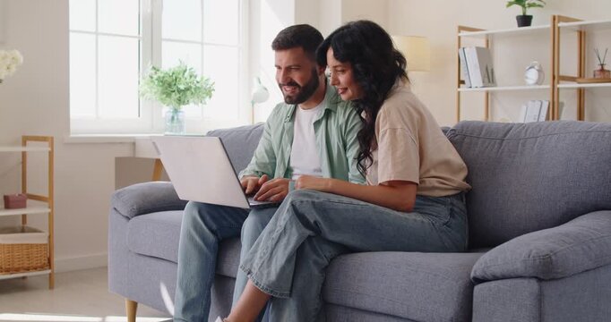 Couple planning online shopping with credit card, using laptop for online purchase at home. Happy woman and man sitting on cozy sofa and browsing, compare prices and planning secure payment together
