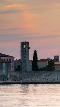 Scenic Sunset View of the Historic Old Town and Stone Bell Tower in Porec Croatia Across the Adriatic Sea Coastline at Dusk with Passing Pedestrians