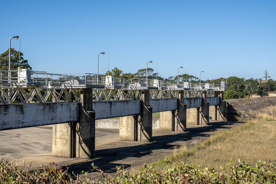 Malmsbury Reservoir water control weir in regional Victoria, Australia featuring multiple concrete piers, steel sluice gates, gantry frames, during drought conditions with a dry empty spillway.