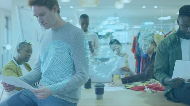 Man in gray sweater reading paper while design team arranging fabrics, overlay emerging over table
