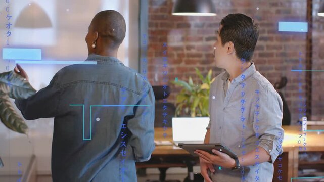 Man gesturing with tablet, woman comparing screens while blue charts on screens aiding design work