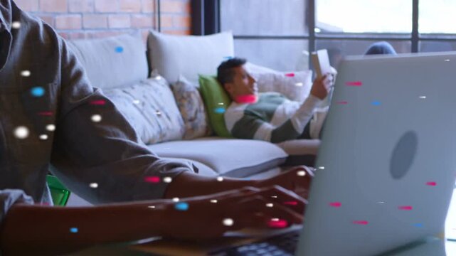 Man typing laptop at table starting remote work, woman reclining reading tablet, particles drifting