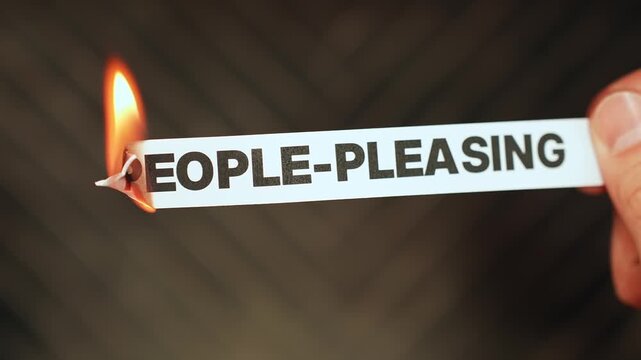 Burning &ldquo;people-pleasing&rdquo; label held by hand, symbolizing setting boundaries, self-respect, and breaking unhealthy approval-seeking patterns.