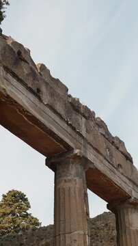 Ancient colonnade in Pompeii, Italy, rising against the sky with weathered Roman columns and stone lintels in a vertical archaeological heritage scene.