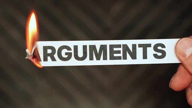 Burning &ldquo;arguments&rdquo; label held by hand, symbolizing peace, reconciliation, calm communication, and moving beyond conflict, tension, and relationship drama.