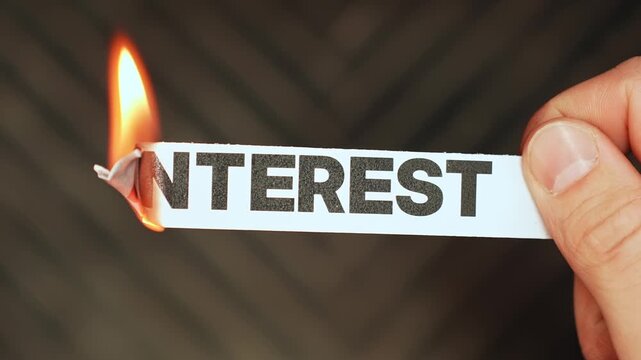 Burning &ldquo;interest&rdquo; label held by hand, symbolizing lower rates, debt relief, cheaper borrowing, and freedom from costly interest payments.