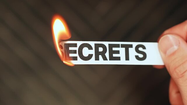 Burning &ldquo;secrets&rdquo; label held by hand, symbolizing honesty, disclosure, truth coming out, and the end of hidden information or private burdens.