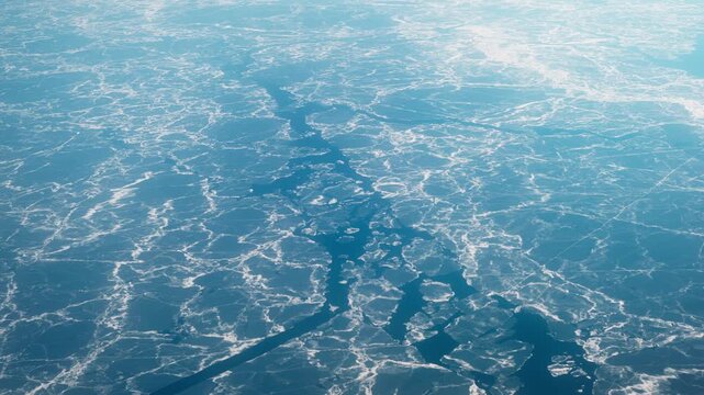 Aerial view of frozen Baltic water near Finland, showing branching white fracture lines across blue sea in a striking abstract winter pattern.