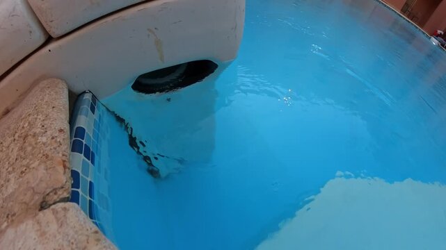 Close-up of a swimming pool return jet and tiled corner with calm blue water, highlighting aquatic facility upkeep, circulation detail, and resort maintenance conditions.