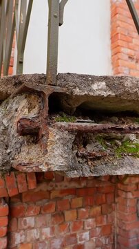 Vertical close-up of a crumbling balcony edge with exposed rusted reinforcement above old brickwork, showing severe decay, unsafe conditions, and neglected property maintenance.