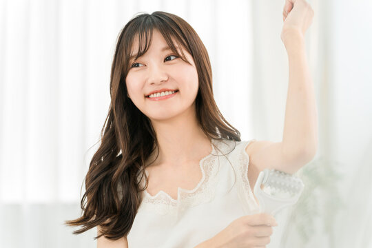 A young woman uses a massage roller on her upper arm at home to loosen up cellulite and lymphatic drainage.