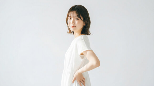 Side view of a Japanese woman standing with hands on hips against white background