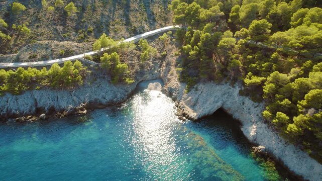 Winding coastal road passes above rocky shores and forested cliffs in summer Kefalonia