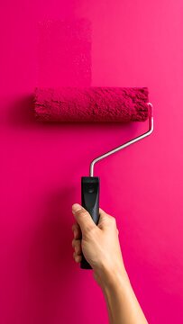 A hand holds a paint roller on a pink wall