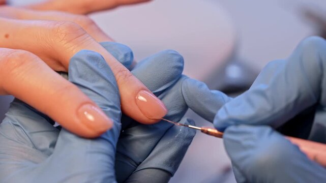 Macro salon close-up of a nail technician perfecting a glossy nude manicure with a fine liner tool, highlighting precise edge refinement and polished minimalist beauty care.