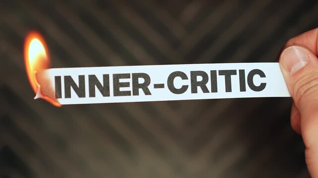 Burning &ldquo;inner-critic&rdquo; label held by hand, symbolizing self-compassion, confidence, emotional healing, and release from harsh self-judgment and negative self-talk.