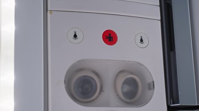 Close-up of an airplane cabin passenger service panel with illuminated call button, reading lights, and air vents inside a commercial aircraft.