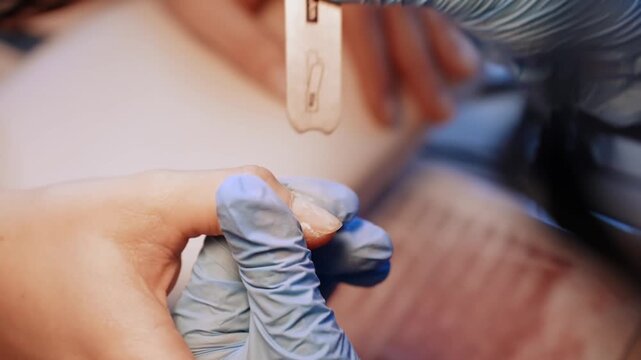 Close-up of a gloved nail technician filing a client&rsquo;s natural fingernail with a disposable emery board during professional salon manicure shaping.
