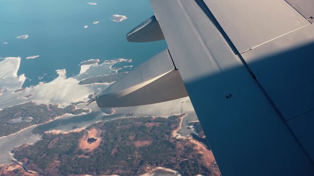 Vintage film-look airplane view over islands and glowing coastline at sunset, capturing a nostalgic travel vibe with wing detail and warm sea reflections.