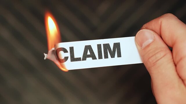 Burning &ldquo;claim&rdquo; label held by hand, symbolizing claim resolution, dispute closure, approved payout, and relief from insurance, legal, or compensation paperwork.