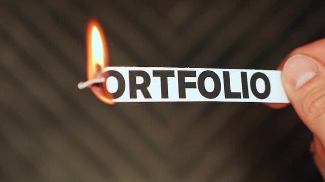 Burning &ldquo;portfolio&rdquo; label held by hand, symbolizing divestment, portfolio reset, asset liquidation, and a strategic shift in investing, business, or creative branding.